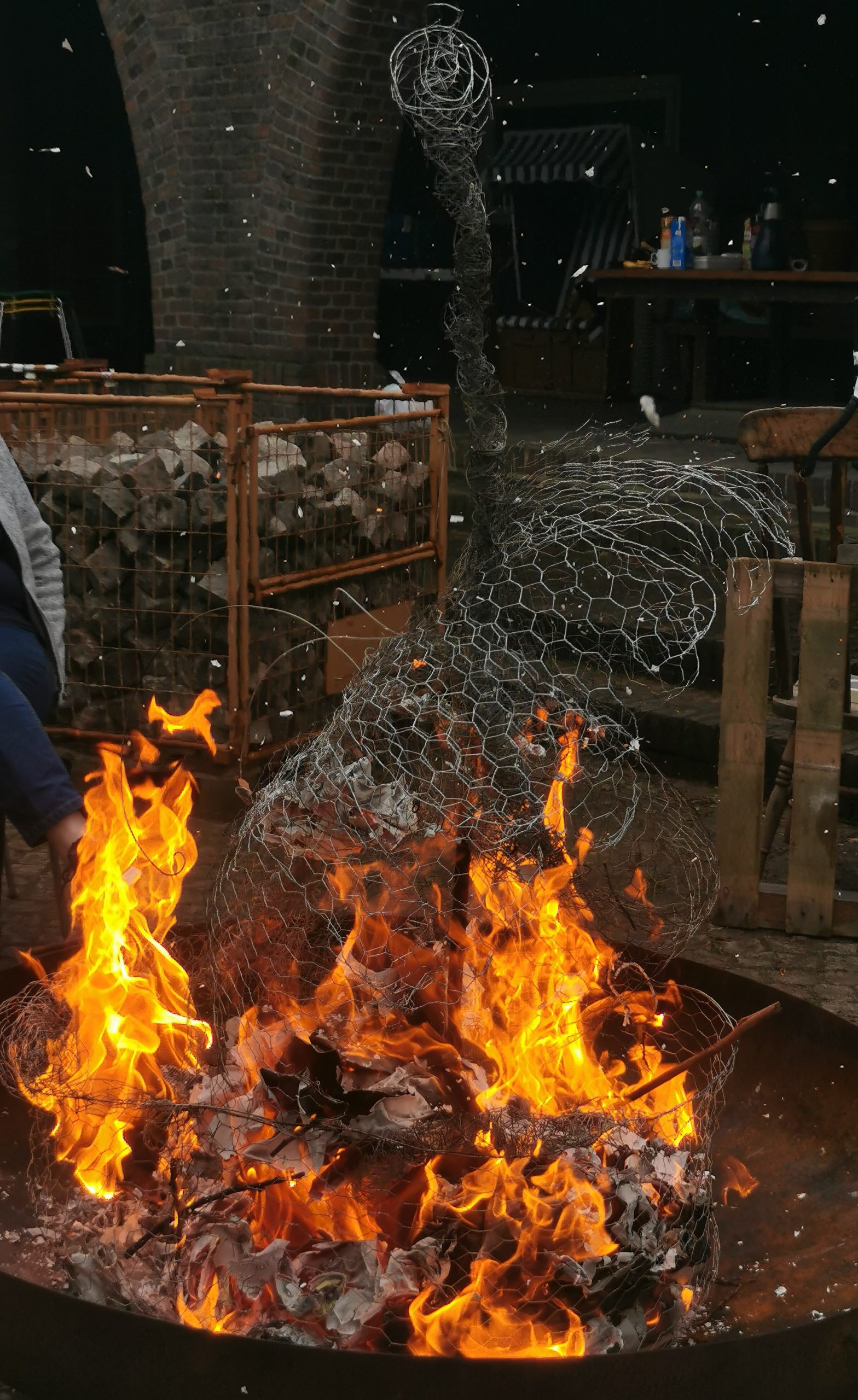 Eine Feuerstelle draußen brennt. In dem Feuer sind Drähte zu sehen.