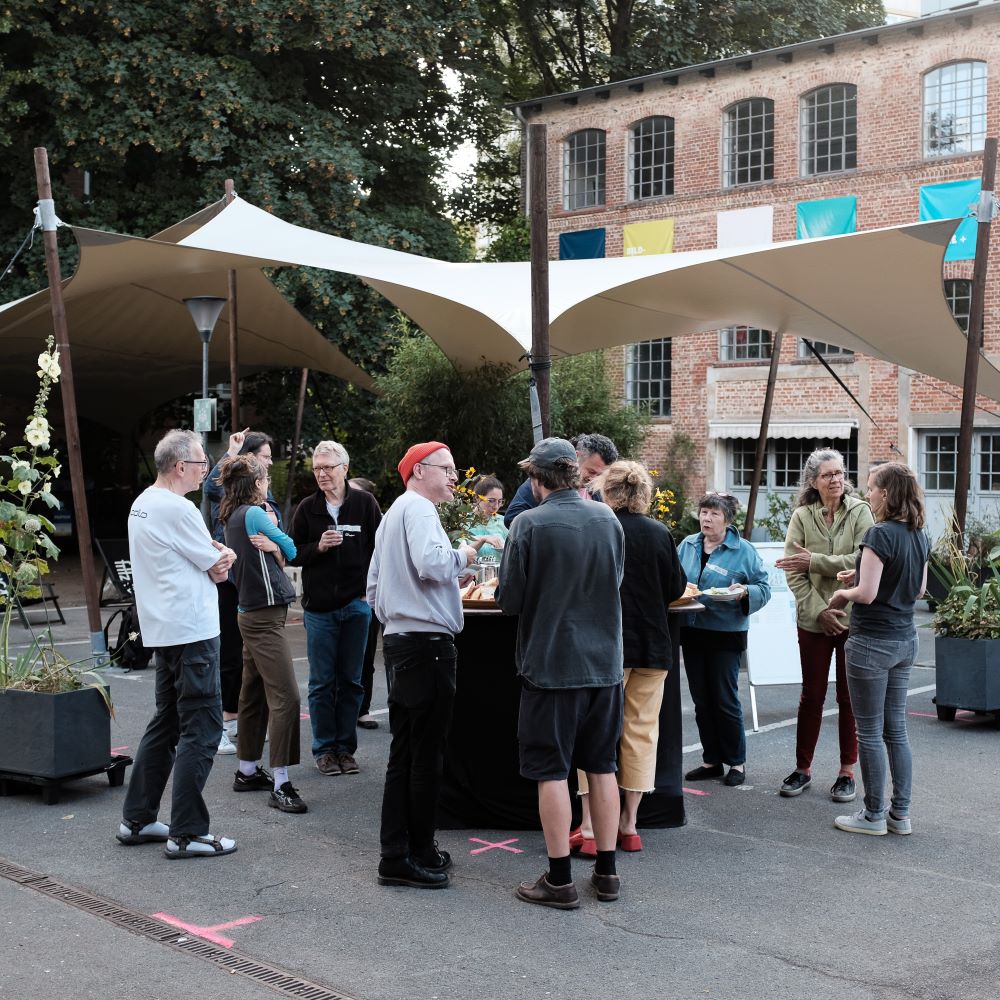 Mehrere Menschen stehen auf dem sommerlichen Goldbekhof und unterhalten sich angeregt