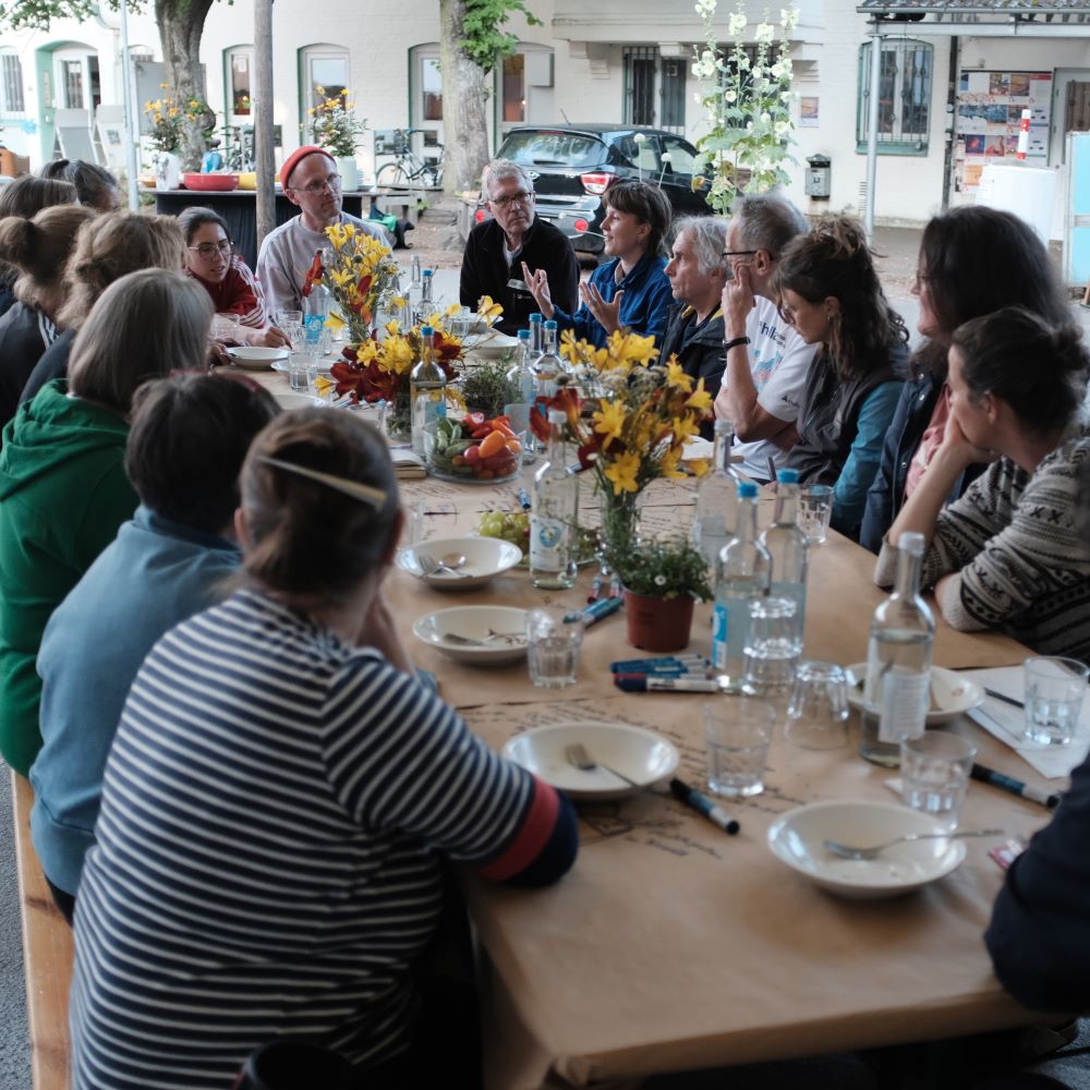 Mehrere Menschen sitzen um einen Tisch herum, eine Frau spricht und die anderen hören aufmerksam zu